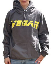 Load image into Gallery viewer, Woman wearing a dark grey hoodie with the word &quot;Vegan&quot; printed in yellow capital letters.
